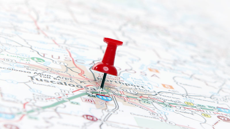A flat map of the city of Tuscaloosa with a red push pin in the center of it.